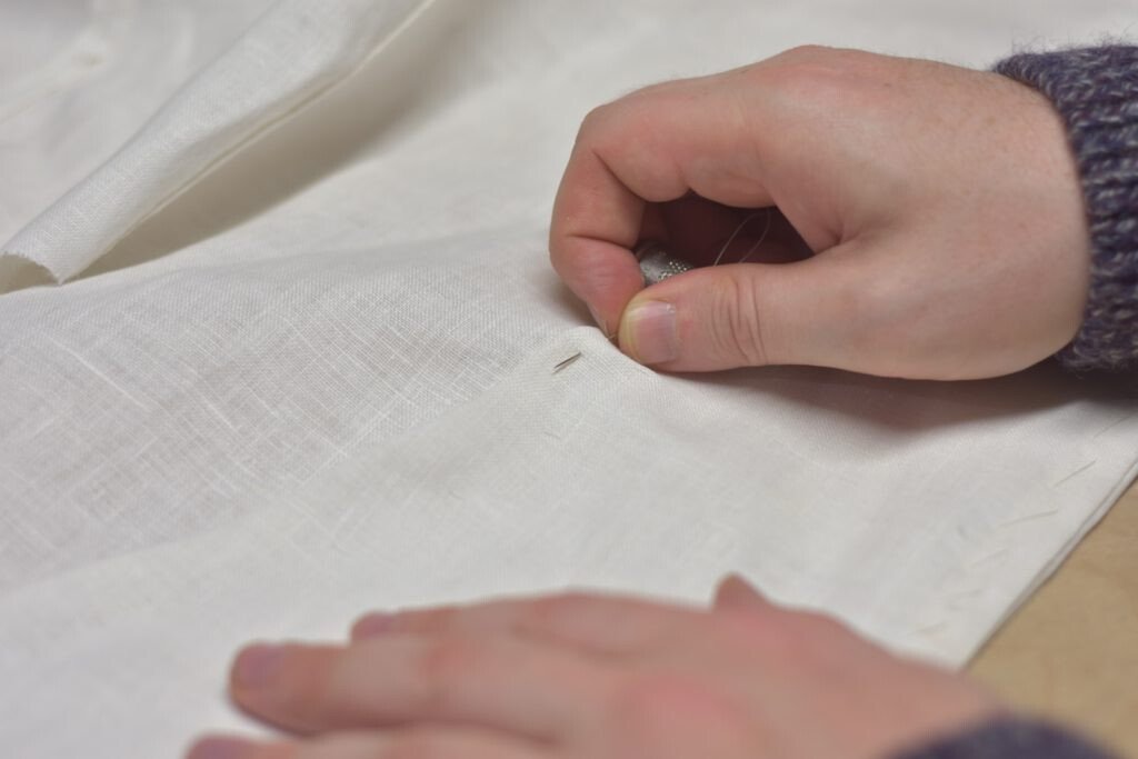 Sewing on coat facings by hand.